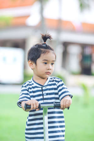Cute little Boy is playing a scooter in a park.He is sadの写真素材