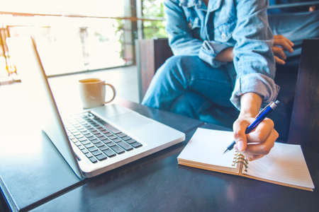 woman using laptop and writing in notepad.