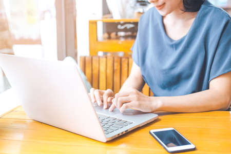 Hand of a businesswoman working from a computer on a wooden desk in an office.