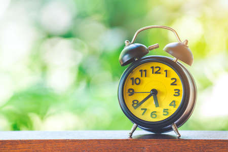 Black Desk Clock with Yellow Screen on Wooden Table background blurred green leaf nature with copy space.の写真素材