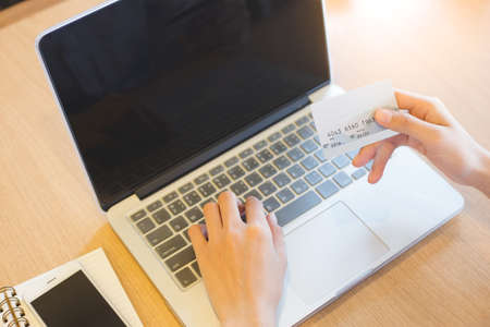 A woman's hand holds a credit card and uses a laptop to shop online.