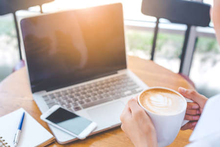 The business woman's hand holds a cup of coffee art and works on a laptop computer in the office.の写真素材