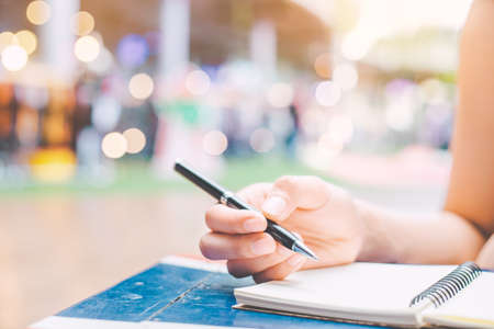 The woman's hand is writing on a blank notepad with a pen on a wooden desk.Film Tone.の写真素材