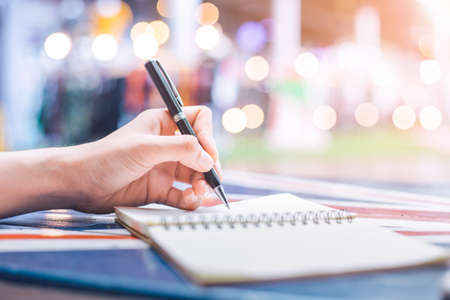 Woman's hand writing on a notebook with a pen on a wooden desk.Background blur backlight