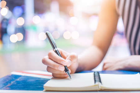 Woman's hand writing on a notebook with a pen on a wooden desk.Background blur backlightの写真素材