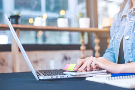 Woman hand works in a laptop computer in the office.On the table are mobile phones. Notepad and penの写真素材