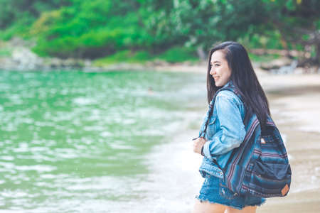 Beautiful Asia woman traveler with a backpack standing on the beach.She looked at the sea and smiled happily.Self-guided travel conceptの写真素材
