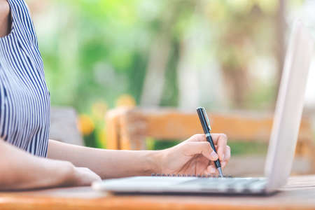 Business woman writing on notepad with a pen In the garden in front of the office.の写真素材