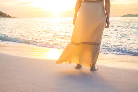 Woman in cream dresses watches the beautiful sunset on the beach.の写真素材