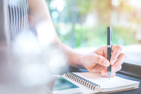 Business woman hand writing on notepad with a pen  in the office.On the table are mobile phones.の写真素材