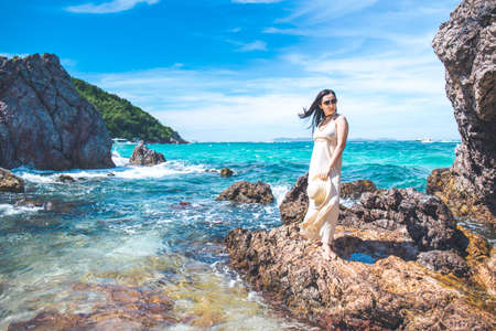 Woman in a cream dress enjoying the beautiful sea on the beach.She stood on the rocks.の写真素材