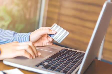 Woman hand holds a credit card and uses a laptop computer to shop online in office.