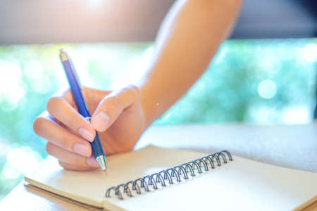 Business woman hand is writing on a note pad with a pen in office.
