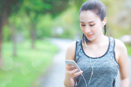 Fitness woman is listening to music from her mobile phone while running in the park.And she was smiling happily.の写真素材