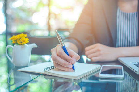 Business woman hand is writing notebook with a pen in the officeの写真素材