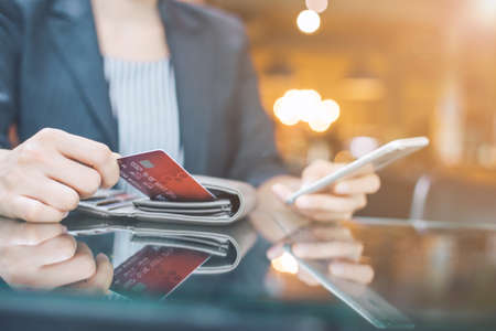 Business women hand are pulling a credit card out of a wallet.And use the phone to check online.Soft focusの写真素材