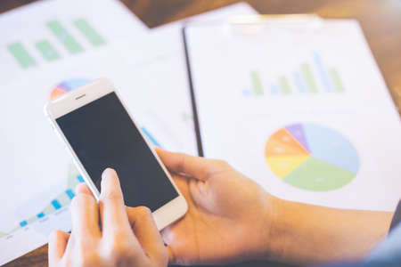 Business work with mobile phones on statistics and business graphs.