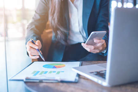 Business woman hand uses a phone to work on charts and graphs that show results.の写真素材