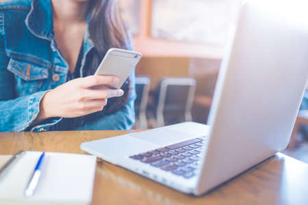 Woman hand uses a smartphone and works in a laptop at offices.の写真素材