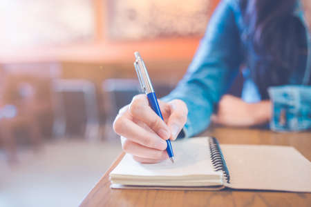 A woman's hand is writing in empty spiral notepad with a pen.