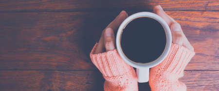 Woman hand in warm sweater holding a cup of coffee on a wooden table background, top view.Web banner.の写真素材