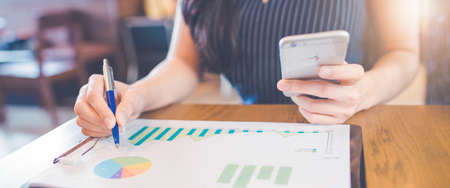 Woman hand writing on charts and graphs that show results with a pen and using a smartphone.Web banner.の写真素材