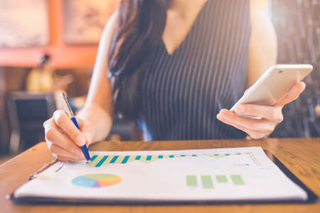 Woman hand writing on charts and graphs that show results with a pen and using a smartphone.の写真素材