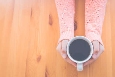 Woman hand in warm pink sweater holding a cup of coffee and heart-shaped handmade on a wooden table...