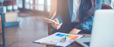 Business woman hand are using cell phones and work on charts and graphs that show results in office.Web banner.の写真素材