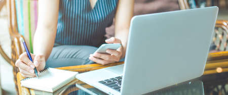 Business woman hand is writing on a notepad with a pen and using a mobile phone.Web banner.