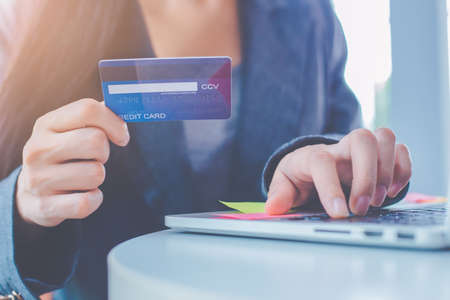 Business women are carrying credit cards and using laptop computers to order products online.