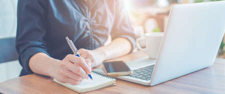 Woman is writing on a notebook with a pen and using a laptop to work in the office.Web banner.の写真素材
