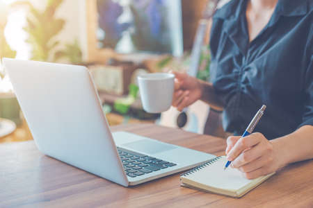 Woman is writing on a notebook with a pen and using a laptop to work in the office.の写真素材