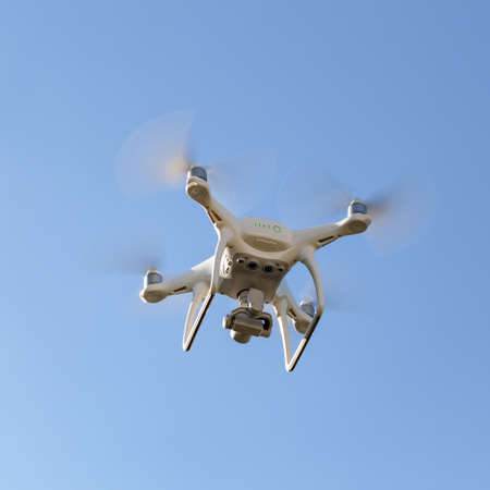 white drone hovering in a bright blue sky.