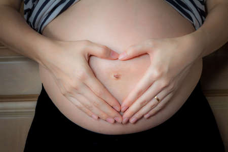 Pregnant Woman with hands in heart shape (love sign) on her baby bump.の写真素材