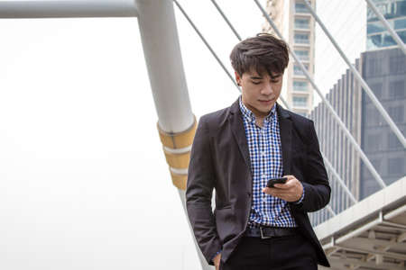 Smart young business man is looking at his mobile phone to check email and news outside officeの写真素材