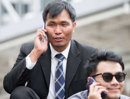 Smart business man  is talking on mobile phone while sitting outside office. He is discussing about business deal with smiling face (select focus)の写真素材