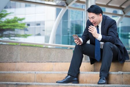 Businessman looking at his smart phone and his face is so happy when stock index is going up and have good news for his projectの写真素材