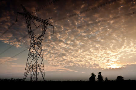 High voltage power pole stands in the middle of the field, with the evening の写真素材