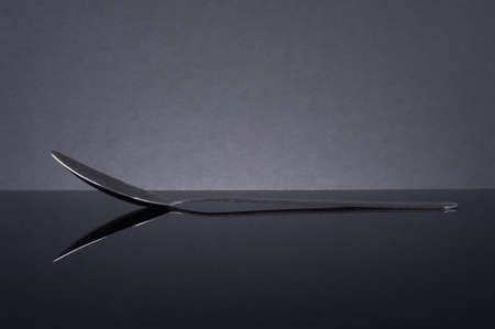 Steel spoon on black surface with reflection.の写真素材