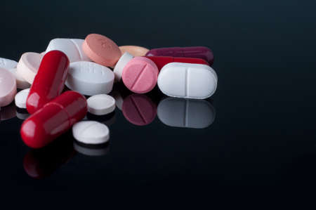 Medical pills and supplement capsule on black table with reflection.の写真素材