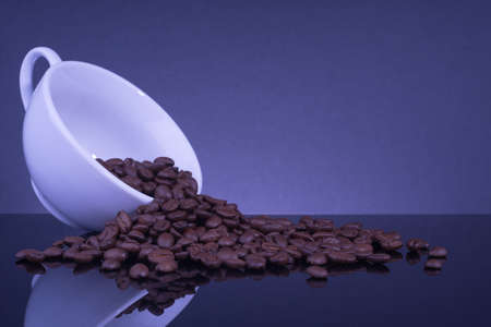 Coffee beans spilled out of a mug on black table with reflection.の写真素材