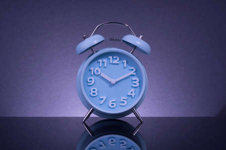 Blue analog alarm clock on black surface with reflection.の写真素材
