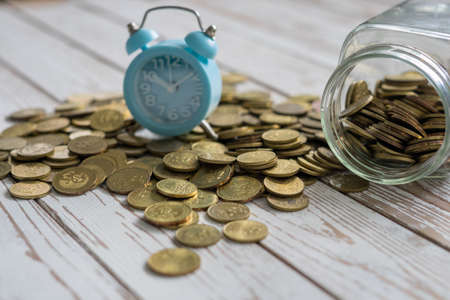 jar of coins with analog alarm clock on vintage wooden table.Financial and investment concept.の写真素材