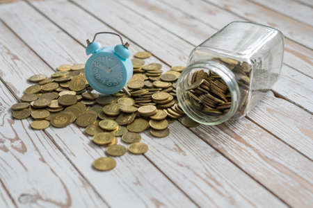jar of coins with analog alarm clock on vintage wooden table.Financial and investment concept.の写真素材