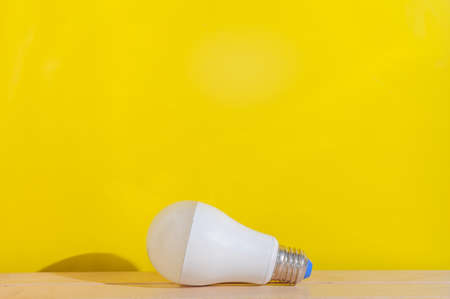 white bulb lying on wooden table with yellow background.の写真素材