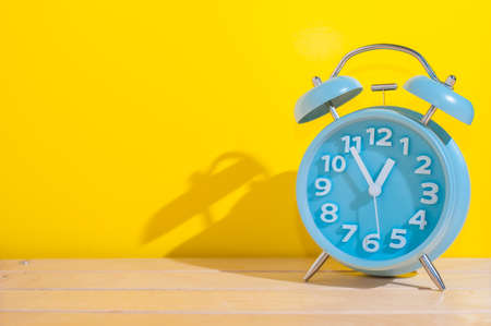 Blue analog alarm clock showing 12 o'clock on yellow background.の写真素材