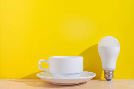 white coffee cup and white bulb on wooden table with yellow background.の写真素材