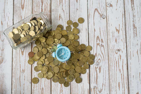 jar of coins with analog alarm clock on vintage wooden table.Financial and investment concept.の写真素材