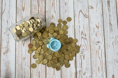 jar of coins with analog alarm clock on vintage wooden table.Financial and investment concept.の写真素材